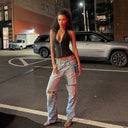A woman stands on a city street at night wearing a Fanic Club black corset-style camisole and light-wash ripped jeans, with cars and brick buildings in the background.